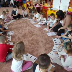 dzieci siedzą na dywanie i wskazują cyfry_ o których jest mowa w piosence.jpeg