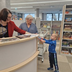 Bibliotekarka podaje książkę chłopcu.jpg