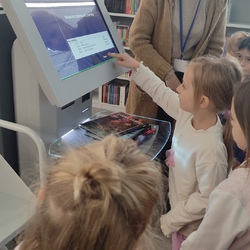 dziewczynka uczy się obsługiwać maszyne do zwrotu książek.jpg